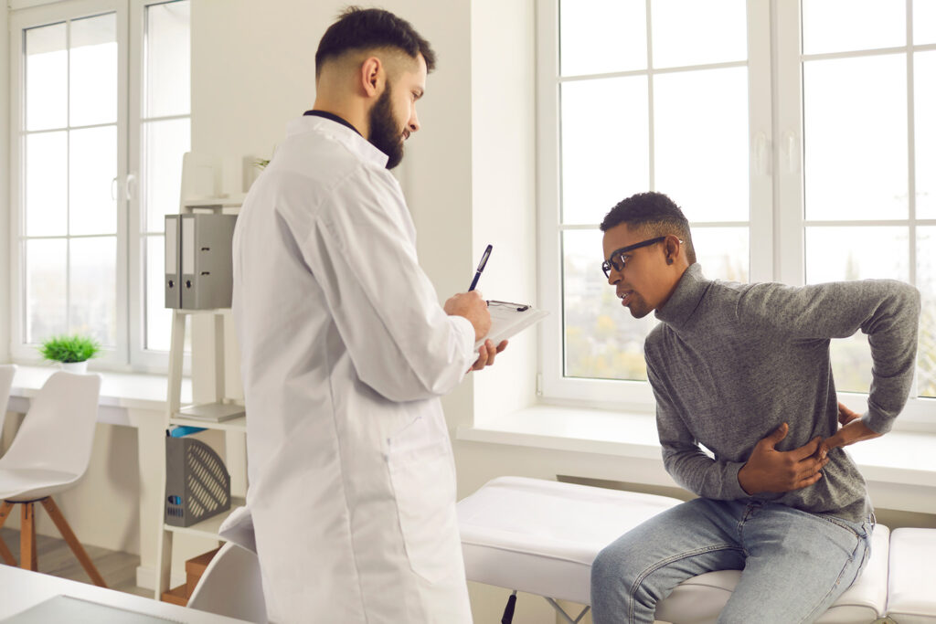 Young African-American patient telling Chiropractor about his backache during visit to hospital